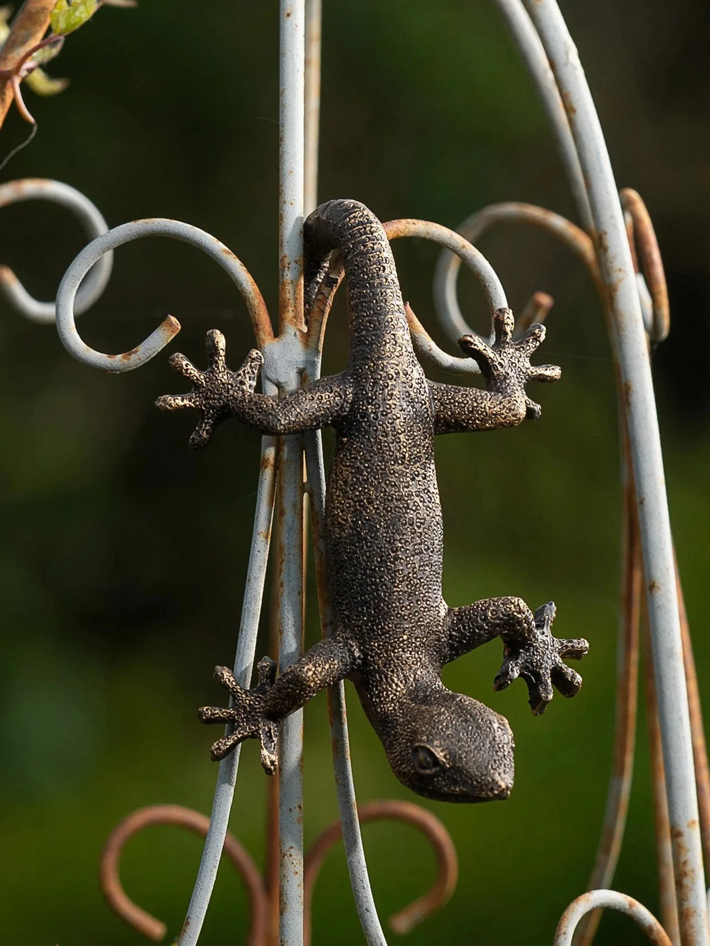 Close-up of the resin gecko figurine on a decorative metal fence outdoors