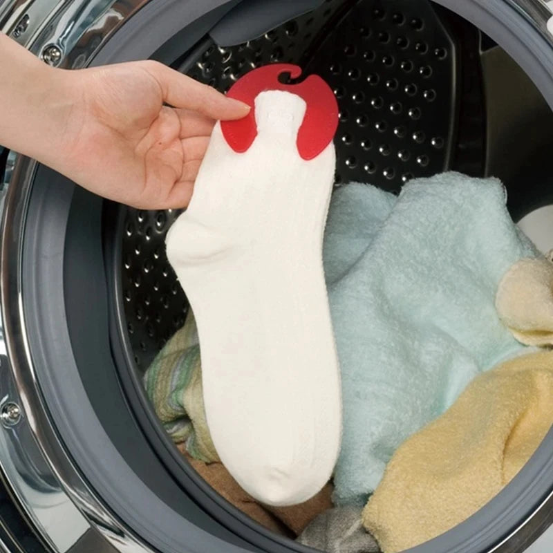 Hand using red sock clip to hold a white sock in front of a washing machine