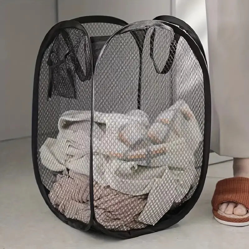 black mesh pop-up laundry basket holding clothes on a bedroom floor