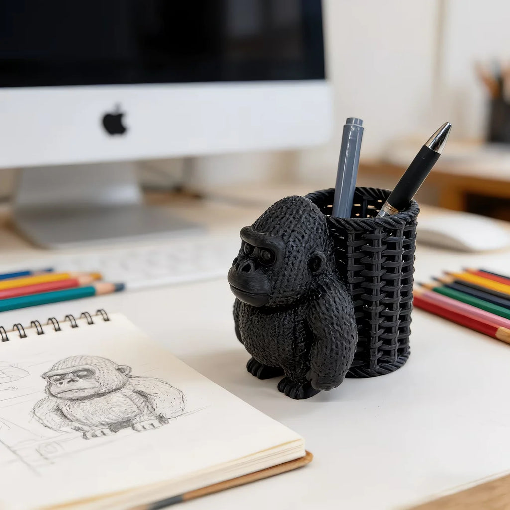 side view of black orangutan pen holder beside sketchbook and computer
