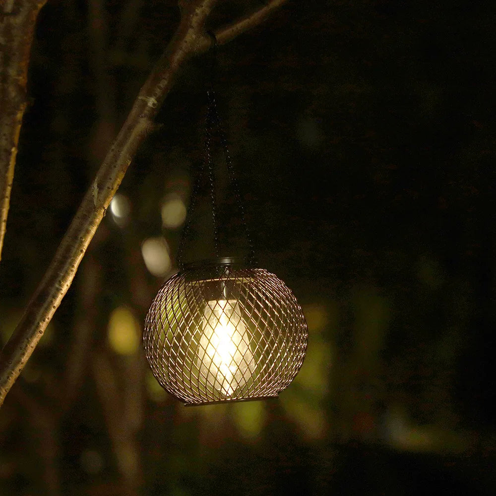 solar mesh lantern hanging from tree, softly lit at night in a garden