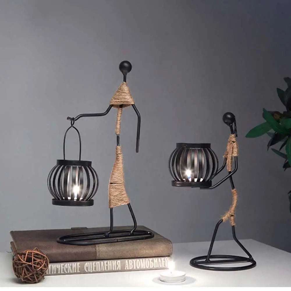 Two metal abstract figure candle holders with twine detail, one holding a lantern, styled on books against a gray wall