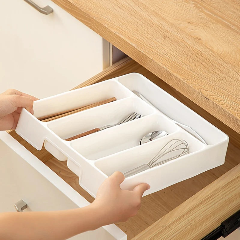 Hands holding a white plastic utensil organizer tray above an open kitchen drawer