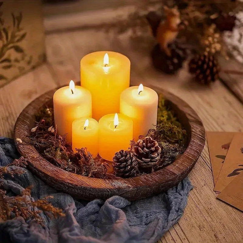 Round wooden tray holding a cluster of pillar candles and pinecones on a wooden table