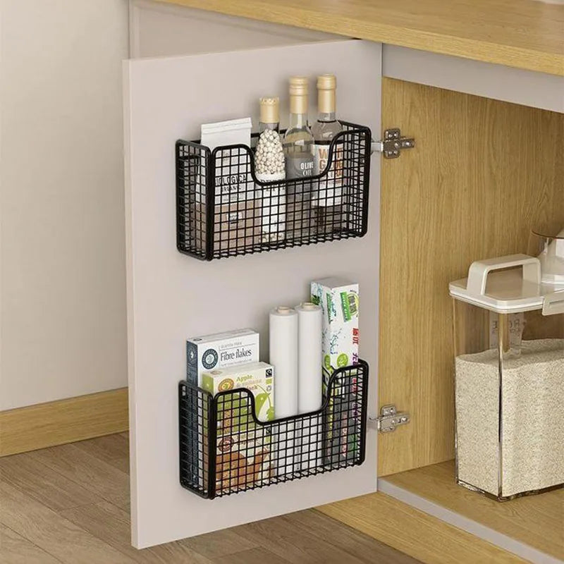 Two black iron storage baskets holding bottles and pantry items on a cabinet door
