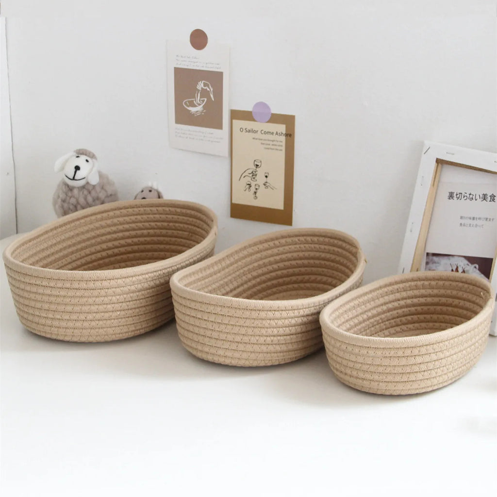 Set of three nested khaki oval cotton rope baskets on a desk, next to decor