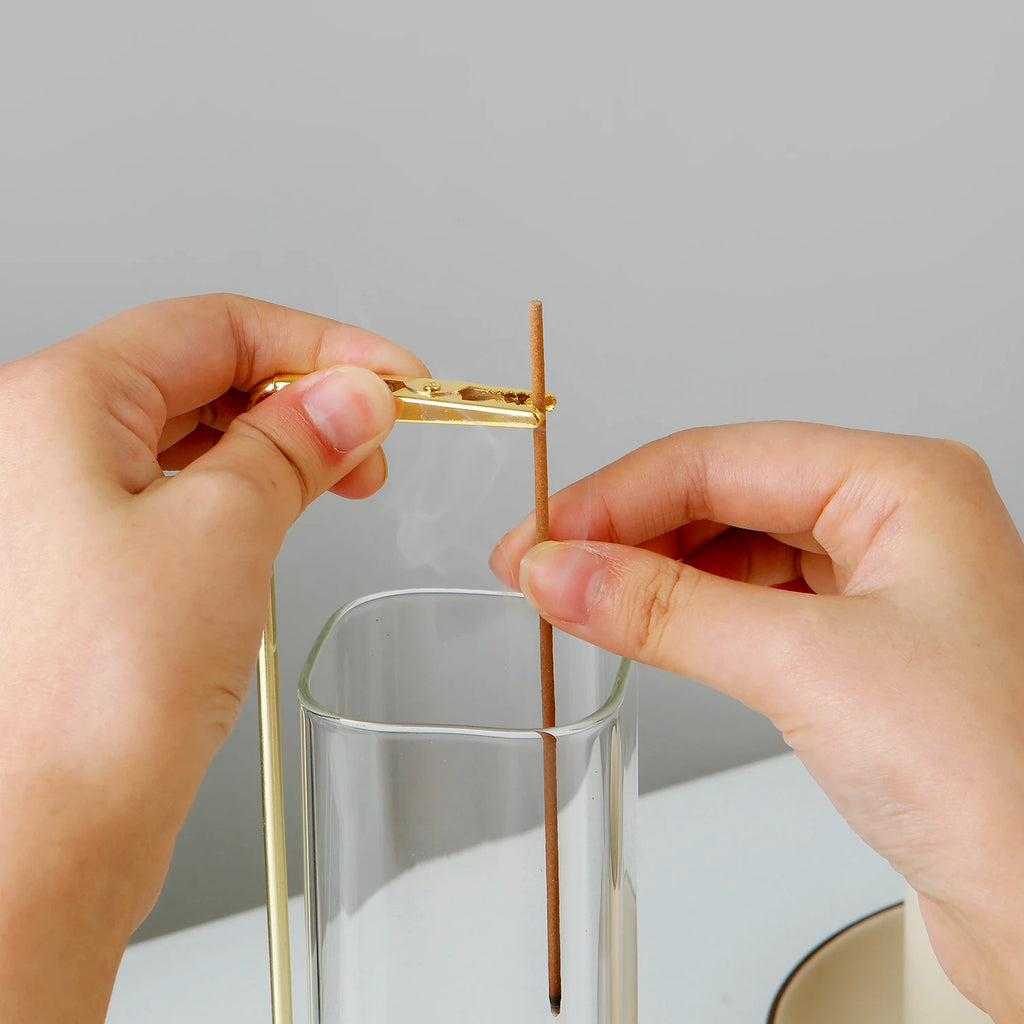 Hands placing incense stick in brass holder above the glass ash catcher