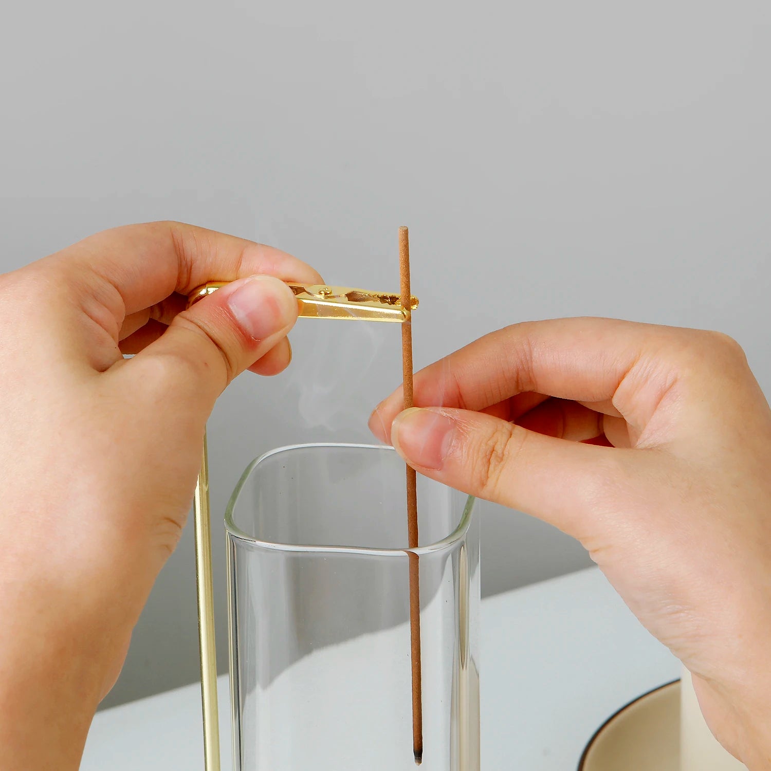 Hands placing incense stick in brass holder above the glass ash catcher