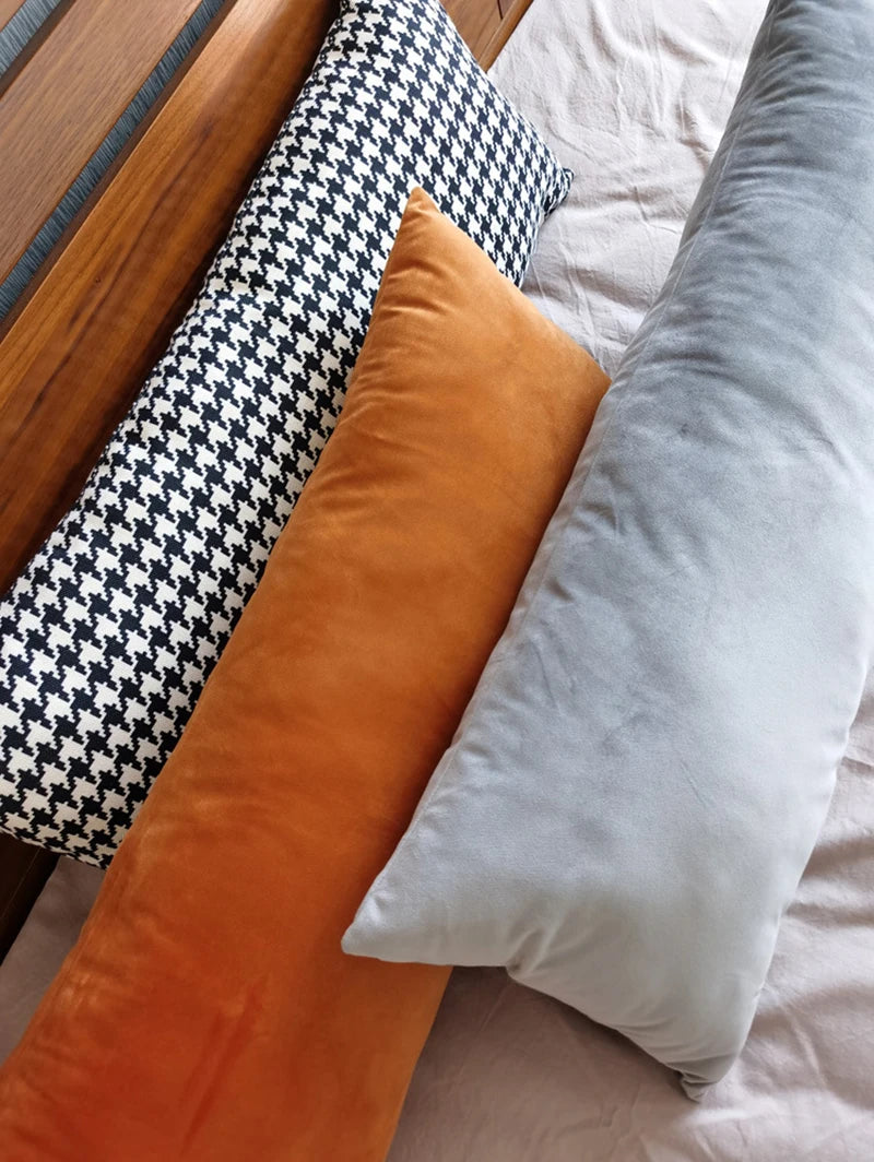 Close-up view of three rectangular pillow covers in a row on a bed: houndstooth, orange velvet, and grey velvet