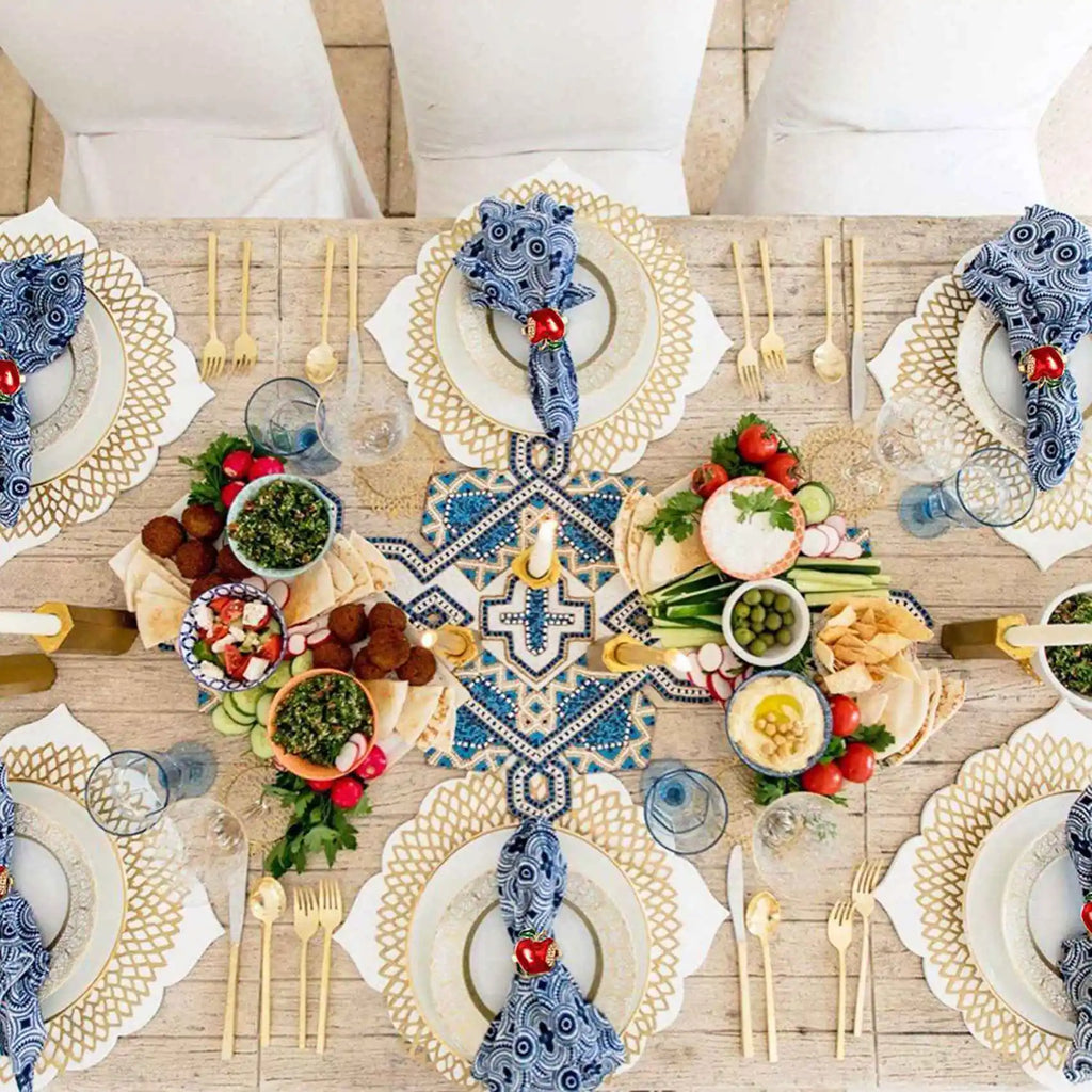 Table setting with blue patterned napkins held by apple napkin rings, surrounded by plates and food for a festive gathering