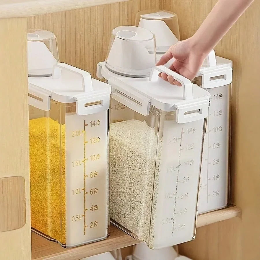 Three clear airtight food storage containers with white lids and handles, filled with grains and stored on a wooden kitchen shelf