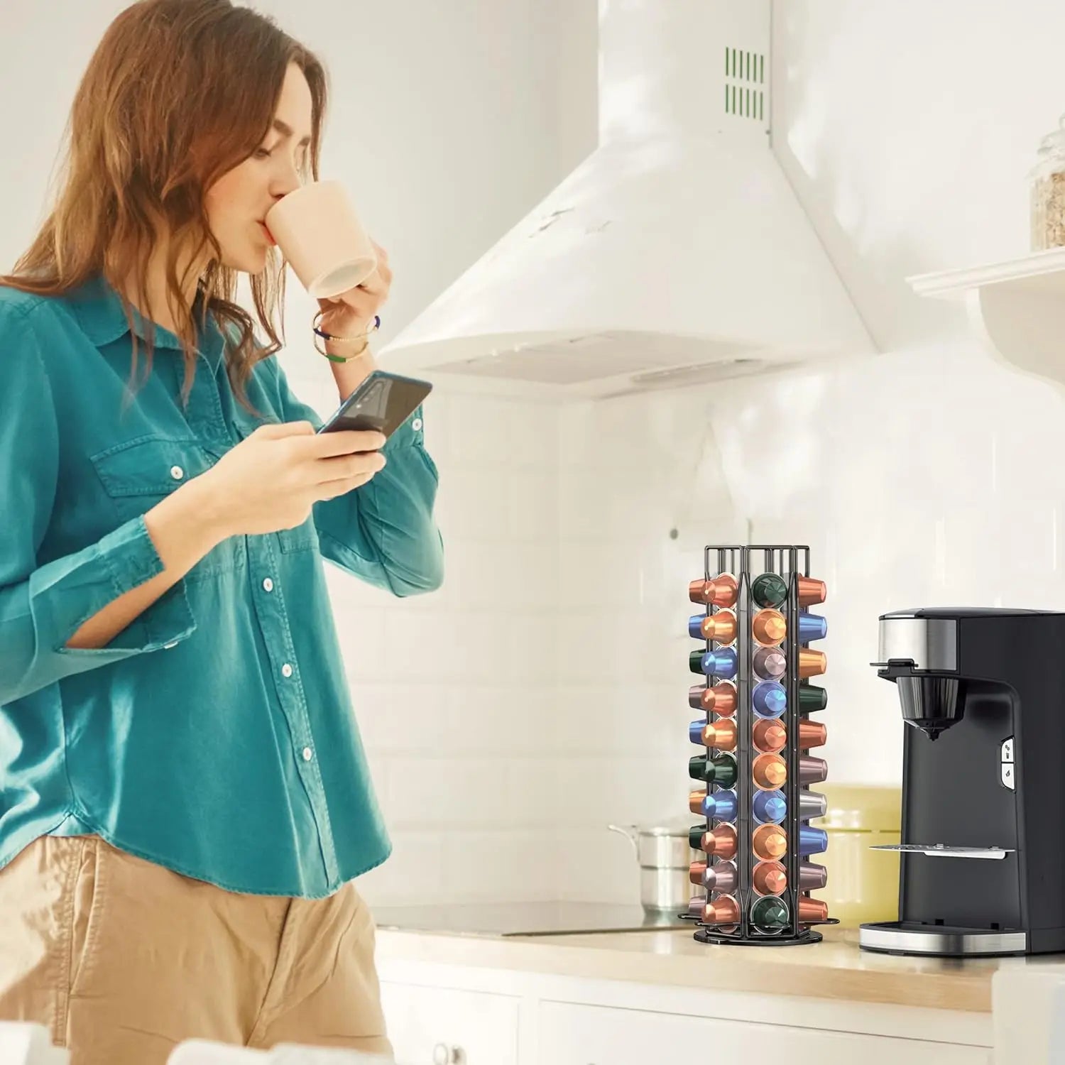 Woman drinking coffee in a kitchen with a rotating coffee pod holder beside a coffee machine