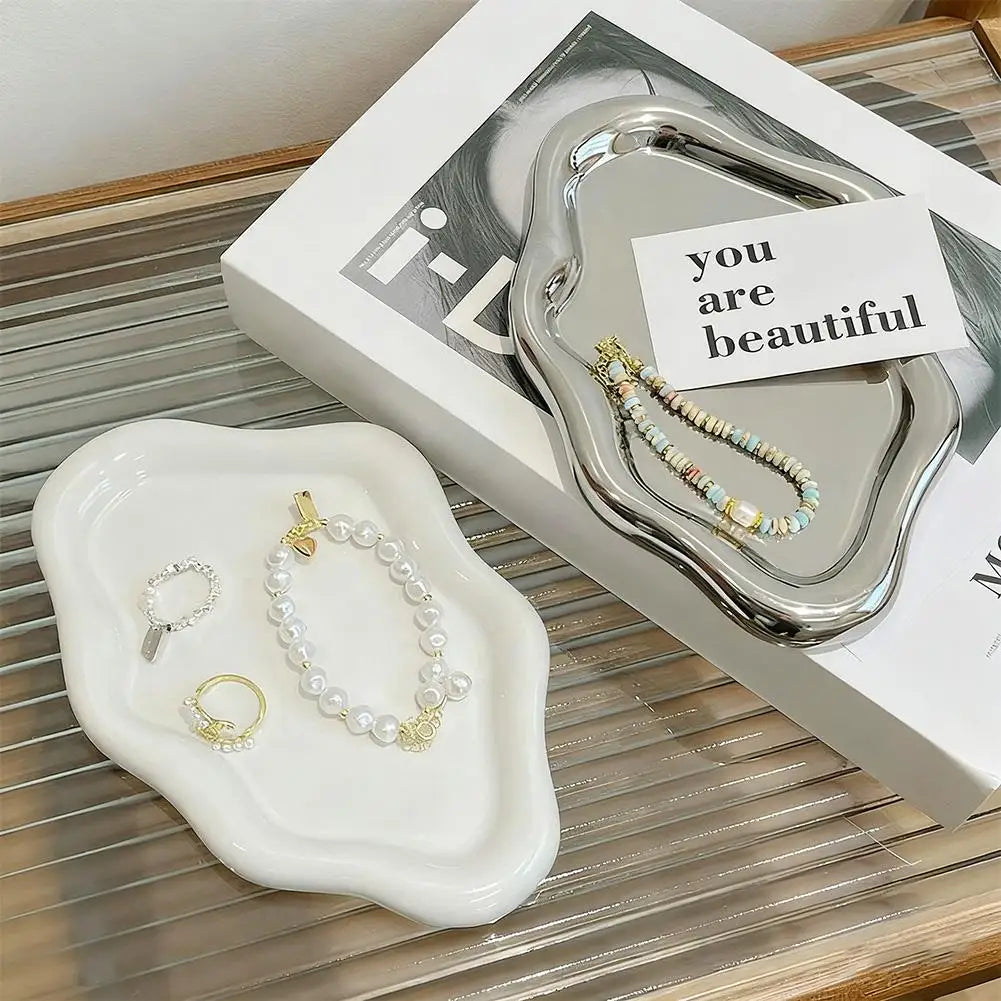 Two cloud-shaped trays in white and silver displayed on a magazine, each holding jewelry