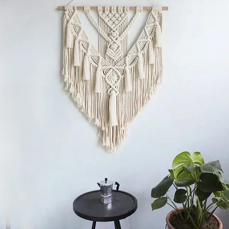 Macrame wall hanging on white wall above a round table with coffee pot and green plant
