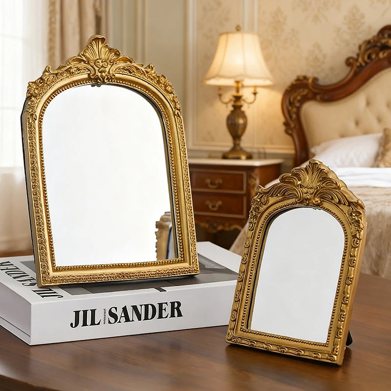 Large and small arched gold mirrors on a bedroom table with decorative accents