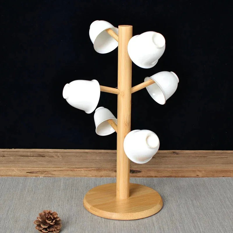 Beige wooden mug tree stand holding six white cups, placed on a neutral tablecloth.