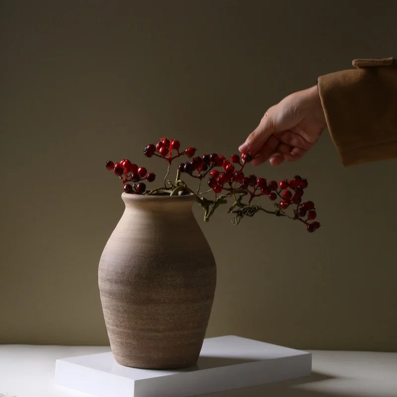 Hand placing red berry stems into rustic brown clay ceramic vase