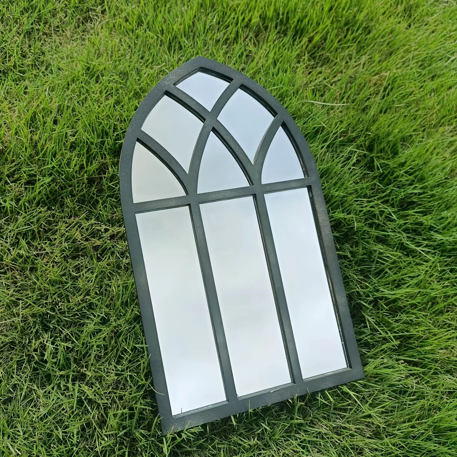 Rounded arch black windowpane wall mirror displayed outdoors on grass