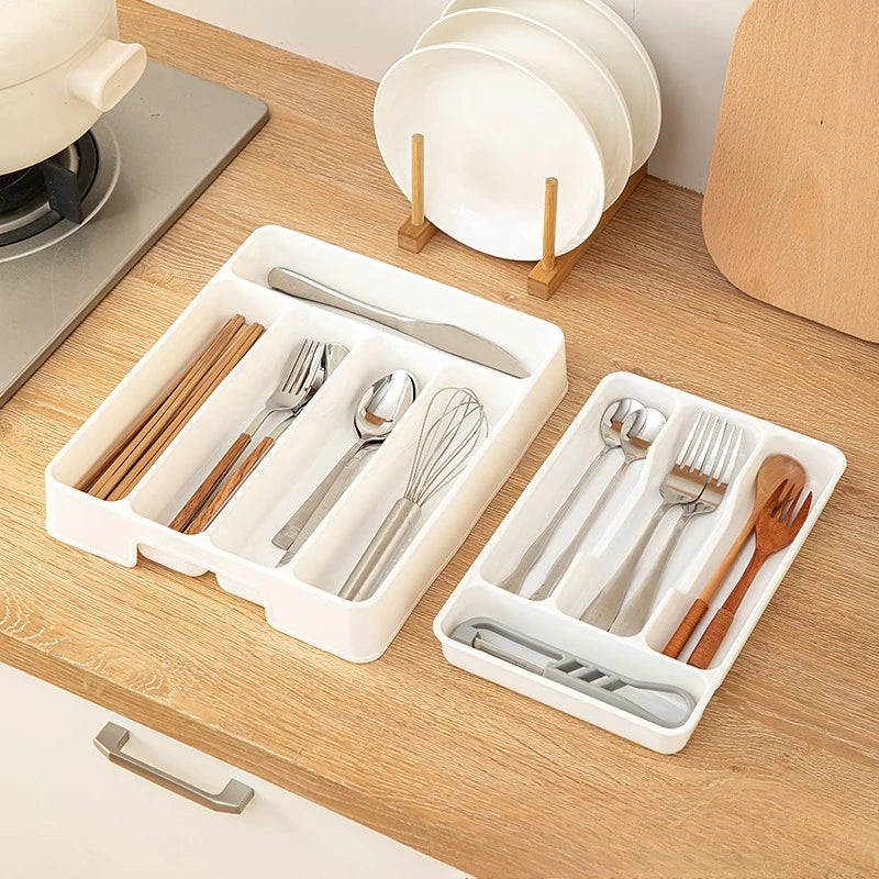 Two white plastic kitchen drawer organizer trays on a countertop, filled with cutlery and utensils