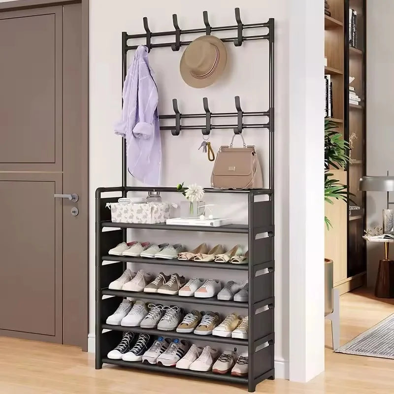 Metal entryway organizer rack with four shelves filled with shoes and upper hooks holding hats and coats next to a front door
