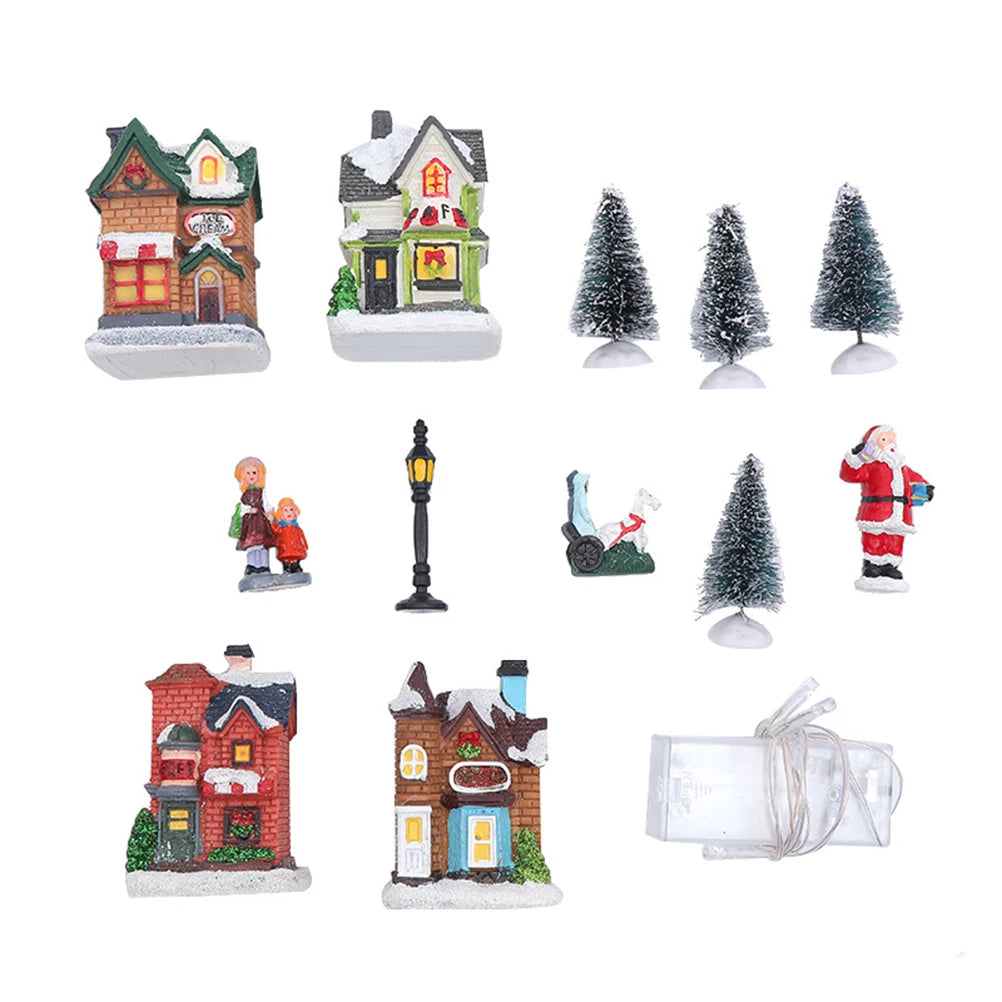 Close-up of individual resin Christmas houses, snow-covered trees, figurines, lamp post, and battery box from village set