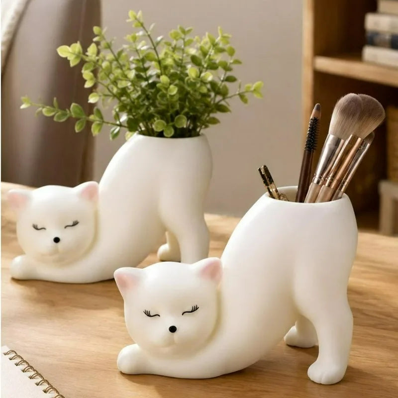 Two white cat planters used for plants and pen storage on a wooden desk