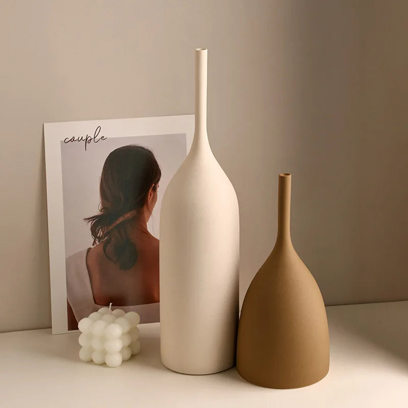 Two slender ceramic vases in light and dark earth tones on a white console with candles