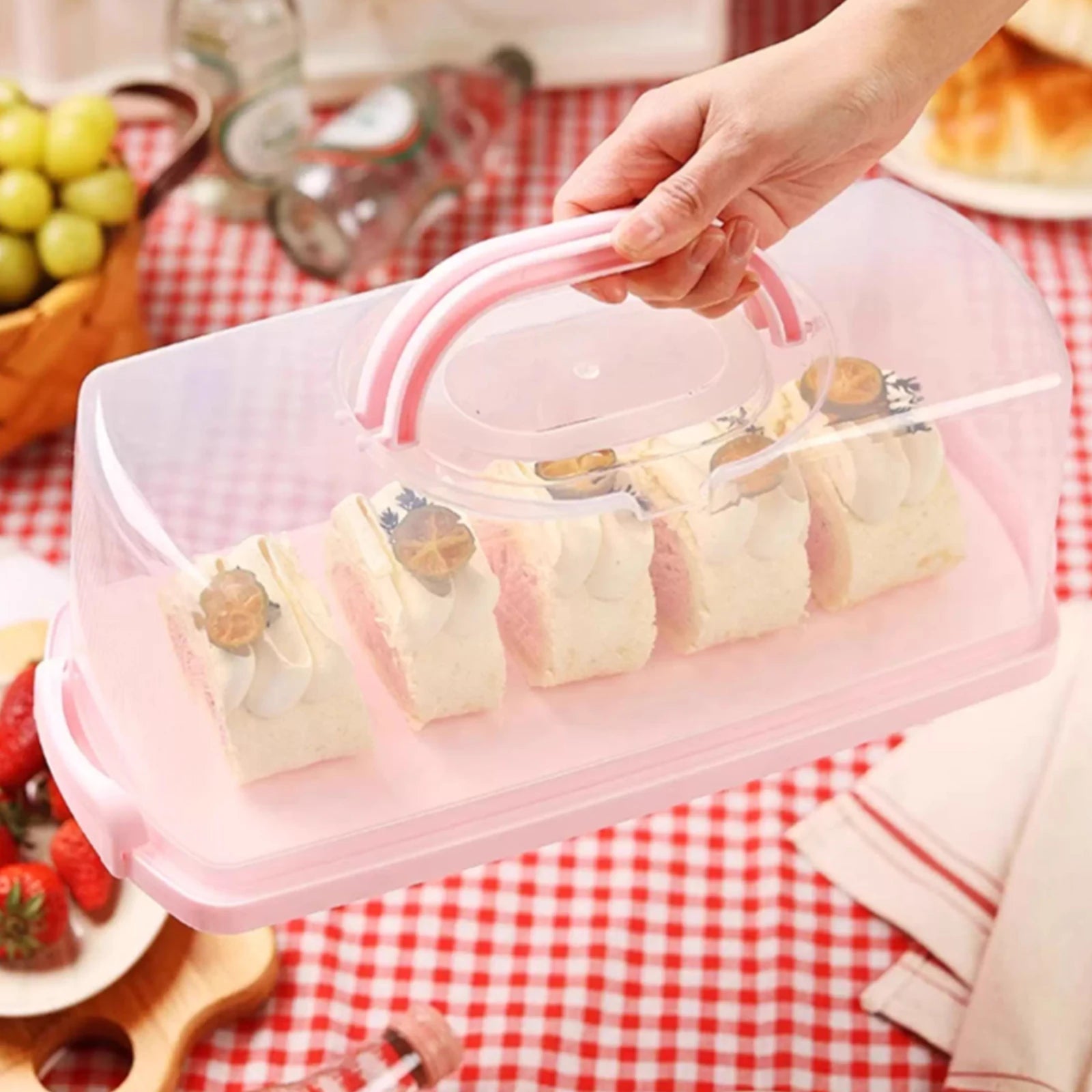 Rectangular bread box with clear lid and pink handle holding cake slices on a kitchen table