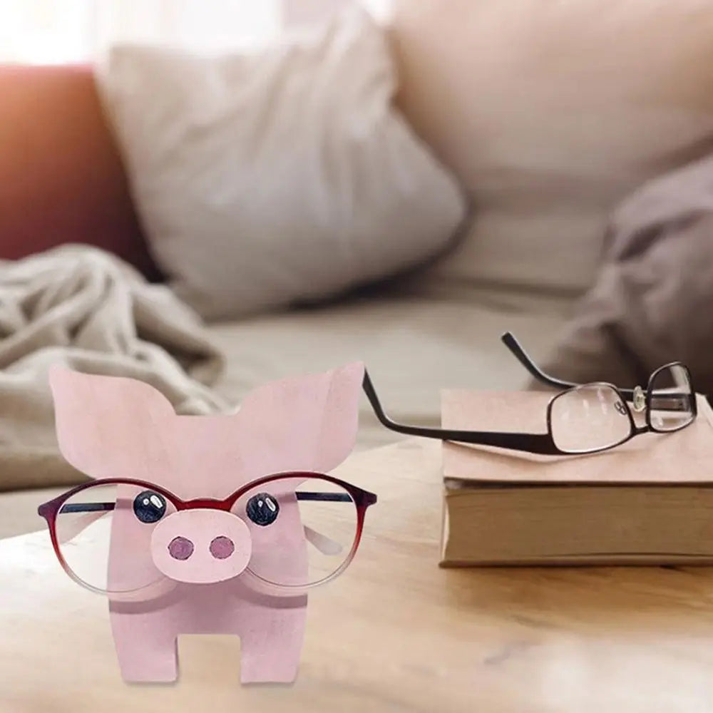 Piglet animal glasses holder on a bedside table next to a closed book and pair of glasses