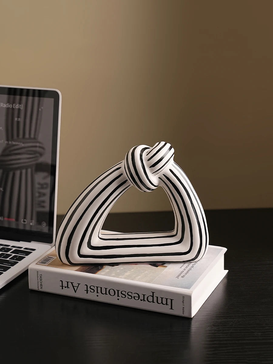 Triangular sculptural knot ceramic vase with black and white stripes displayed on a book next to a laptop.