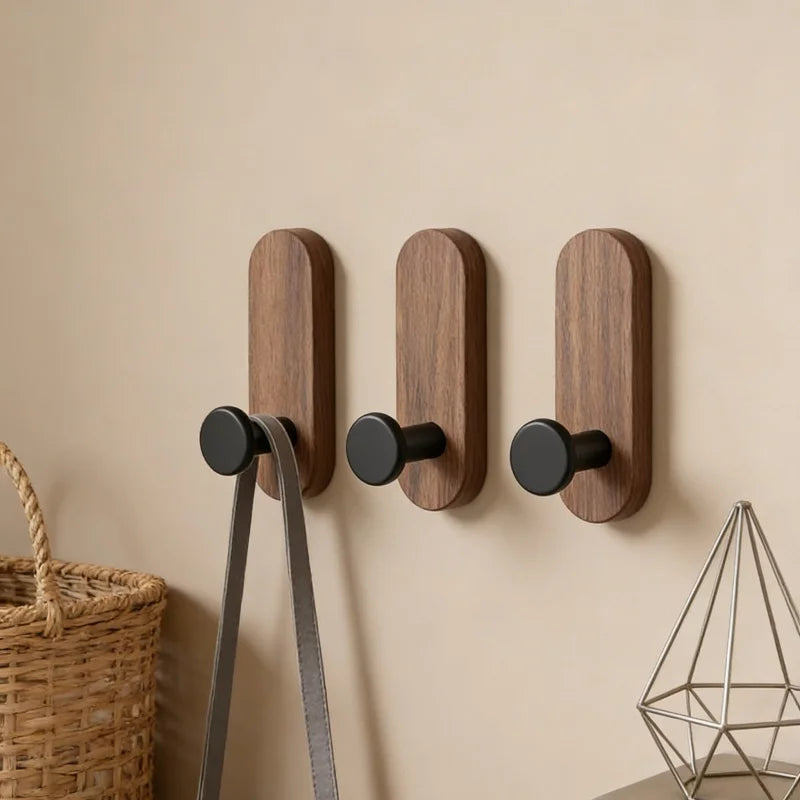 Three dark wood wall hooks with black pegs holding a bag, with basket and decor nearby