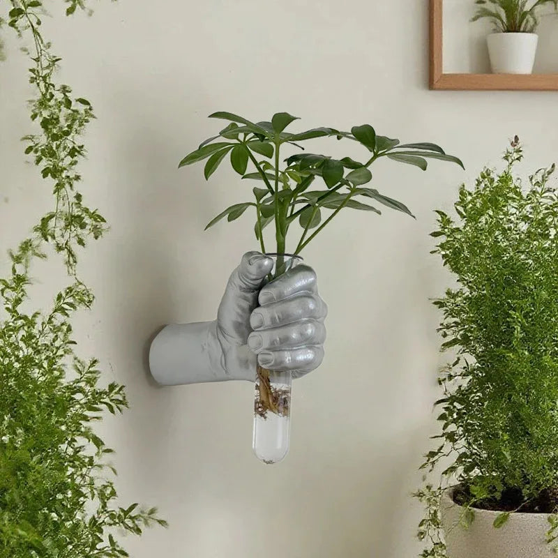 Silver fist-shaped wall vase displaying green cuttings among houseplants
