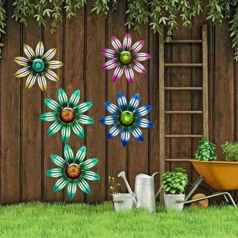 Colorful metal flower wall art displayed on a wooden garden fence with plants and garden tools