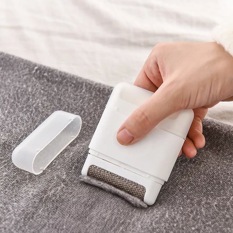 White lint remover brush in use on a gray sweater, cap placed beside