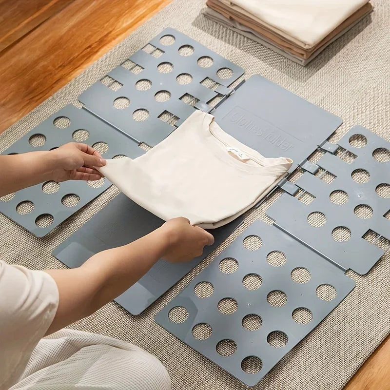 Hands folding a shirt using a blue plastic folding laundry board on a rug