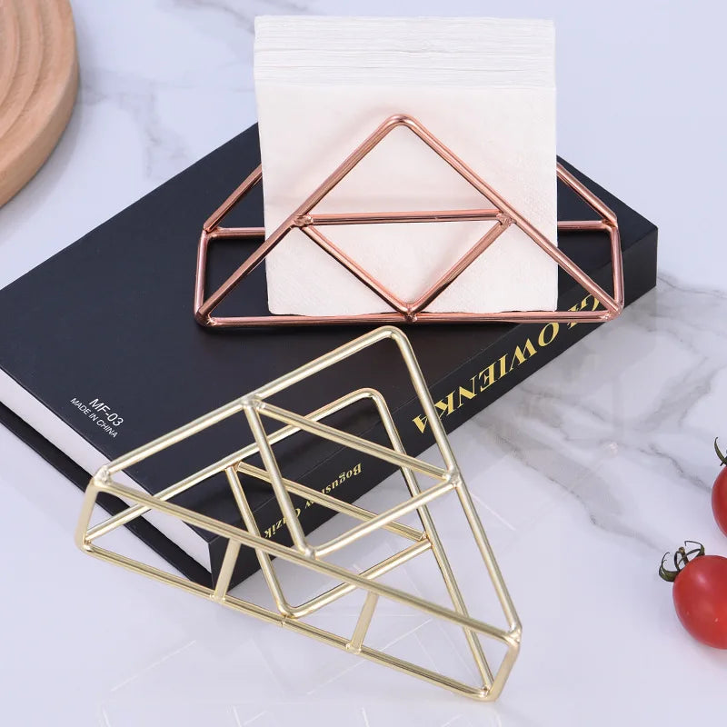 Gold and rose gold triangle metal napkin holders, one holding napkins on a book