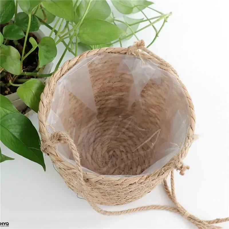 Top view into empty woven jute hanging basket planter lined with plastic, shown on a table with green plant nearby