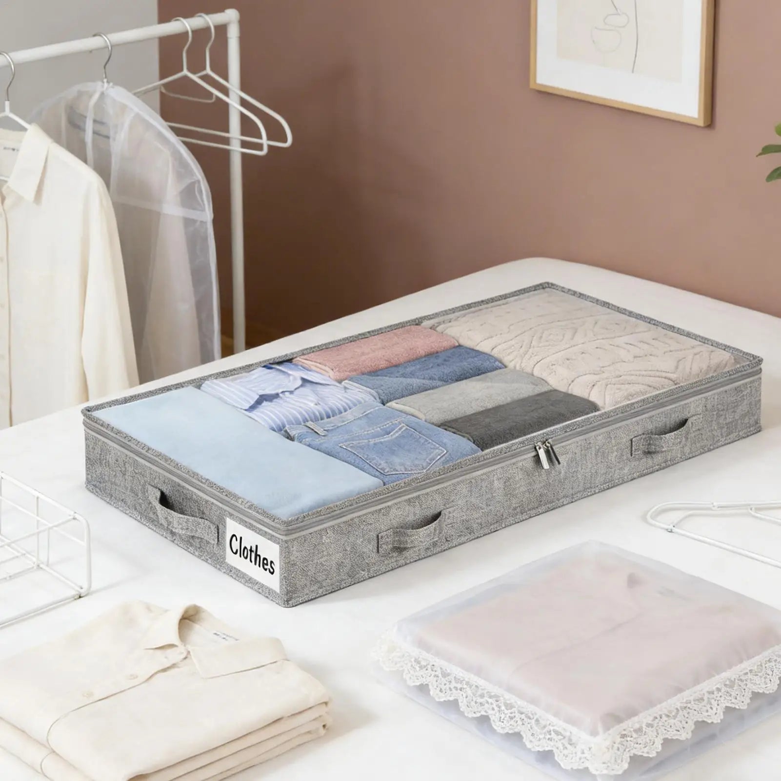Rolling underbed storage bin with clear lid filled with folded clothes on a white bed