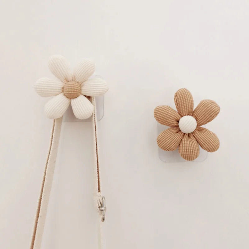 Pair of daisy fabric flower wall hooks in beige and khaki on a white wall, one holding a strap