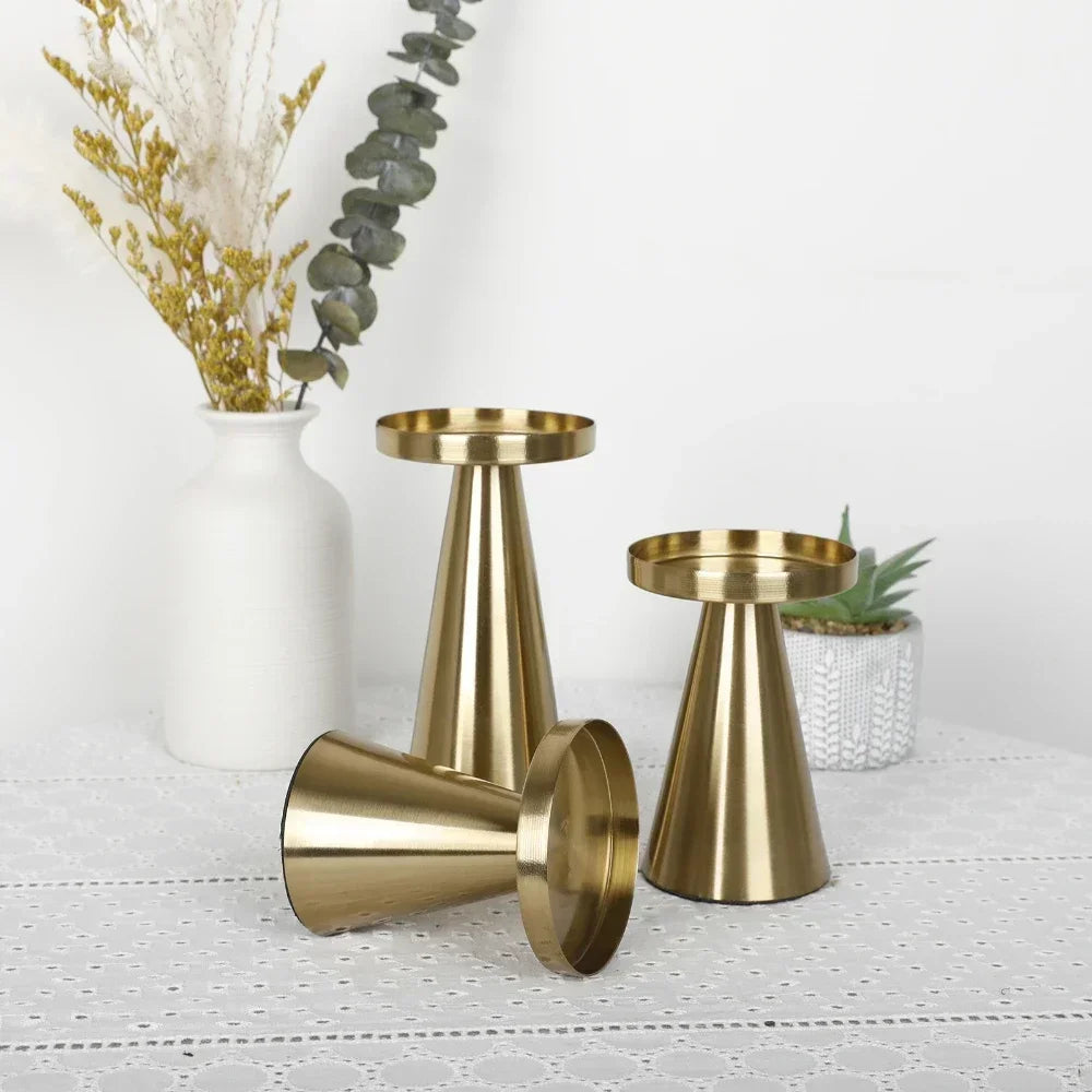 Three gold cone-shaped metal candle holders without candles, shown from different angles on a lace tablecloth.