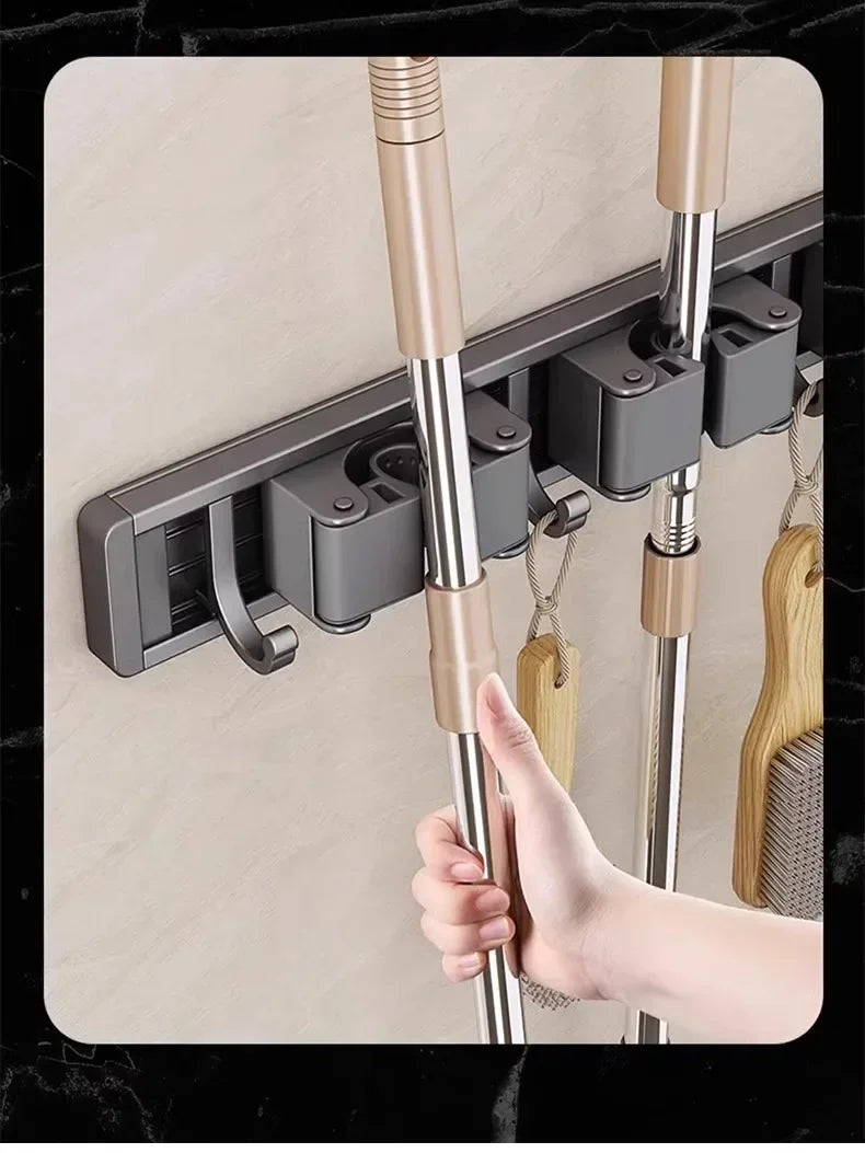 Hand placing a mop onto the wall-mounted gripper rack with hooks and handles organized