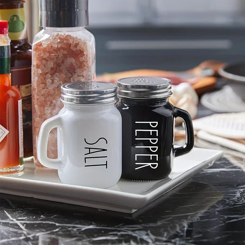 Black and white glass salt and pepper shakers with handles on kitchen counter