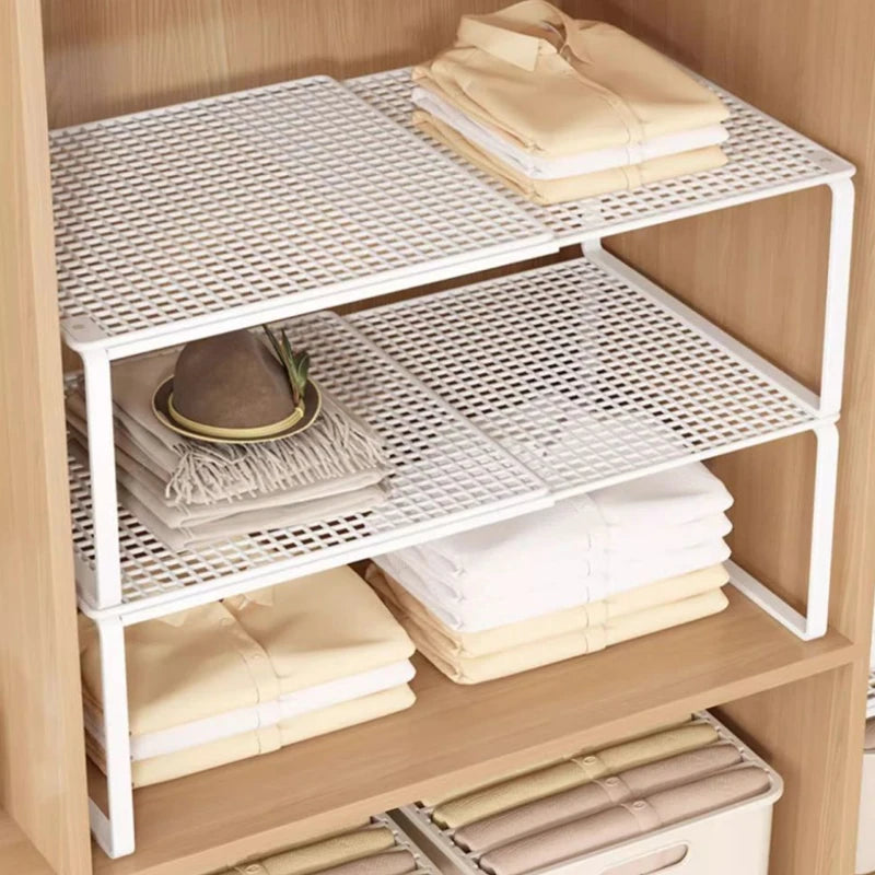 Stacked and staggered white metal shelf organizers in a closet with folded clothes and accessories