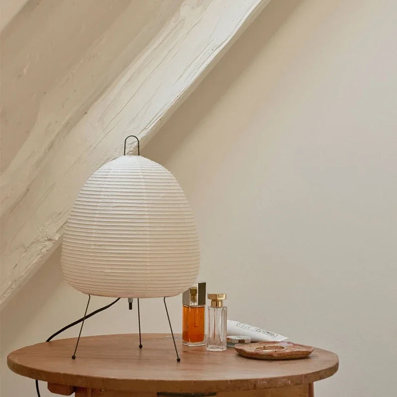 Unlit rice paper table lamp on a round wooden side table under a slanted ceiling