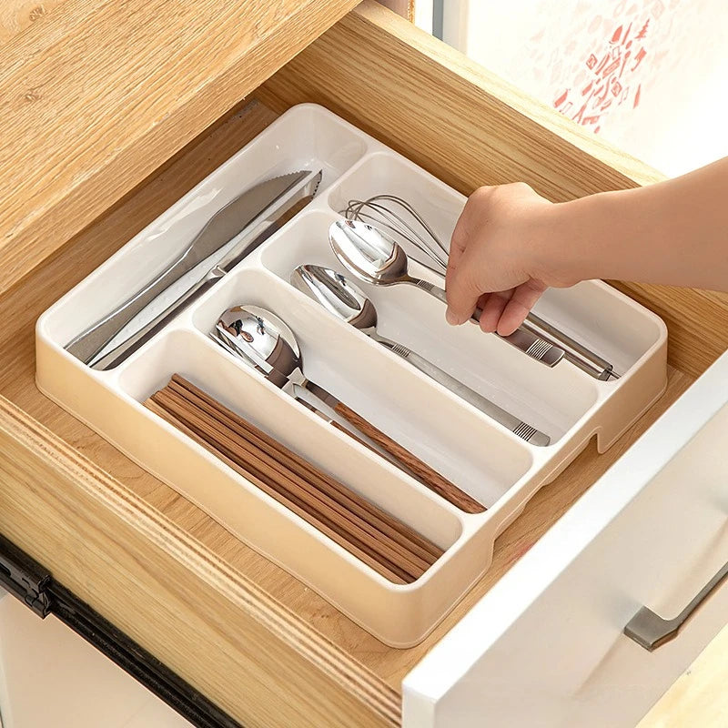 Hand placing utensils into a white kitchen drawer organizer tray inside a wooden drawer