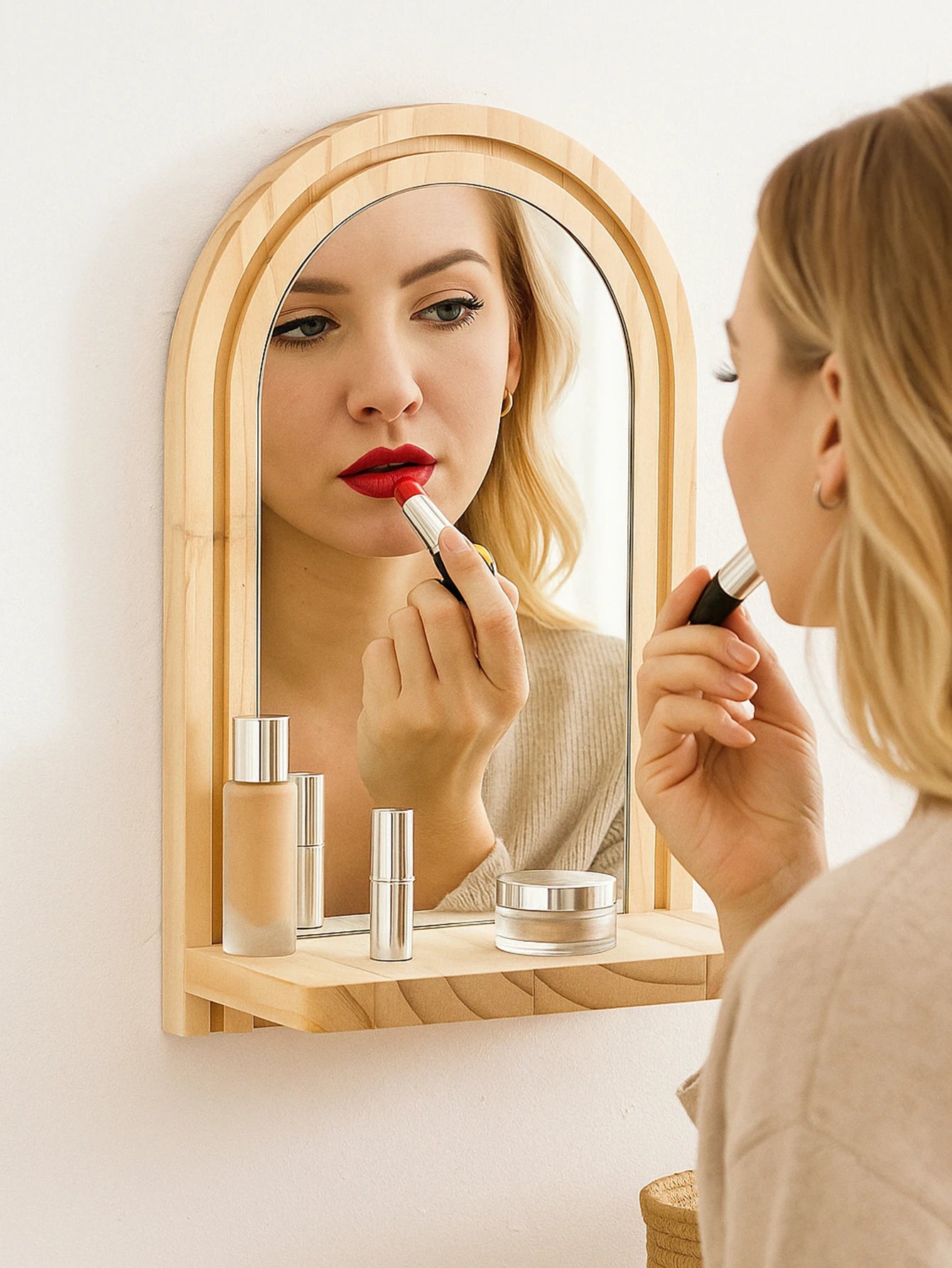 arched wooden mirror with shelf on the wall, shown as a makeup station with a person holding lipstick and cosmetics on the shelf