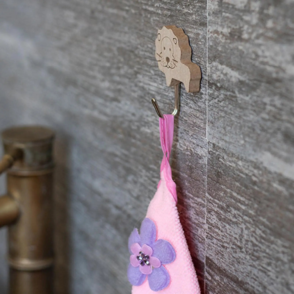 lion-shaped bamboo wall hook mounted on gray tile wall holding a pink towel with a purple flower