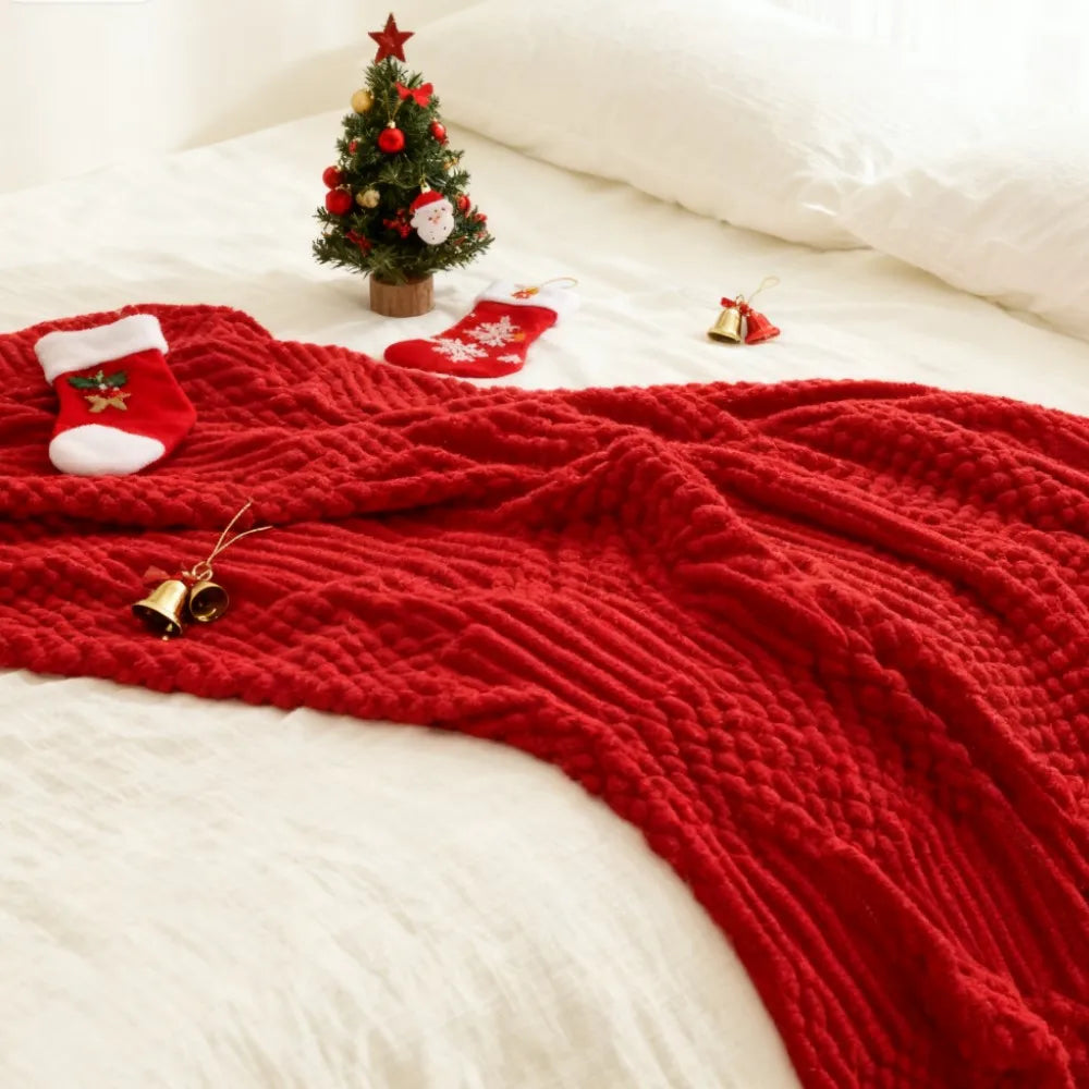 Red textured knit throw blanket laid across a bed with stockings and mini holiday tree