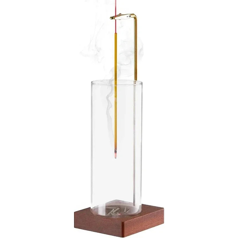 Glass tube incense holder with wood base and upright incense stick, smoke visible inside cylinder