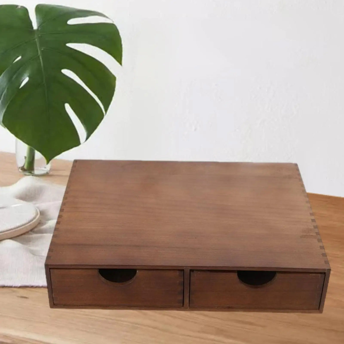Brown wooden two-drawer organizer closed, on a light wood surface with a green leaf nearby